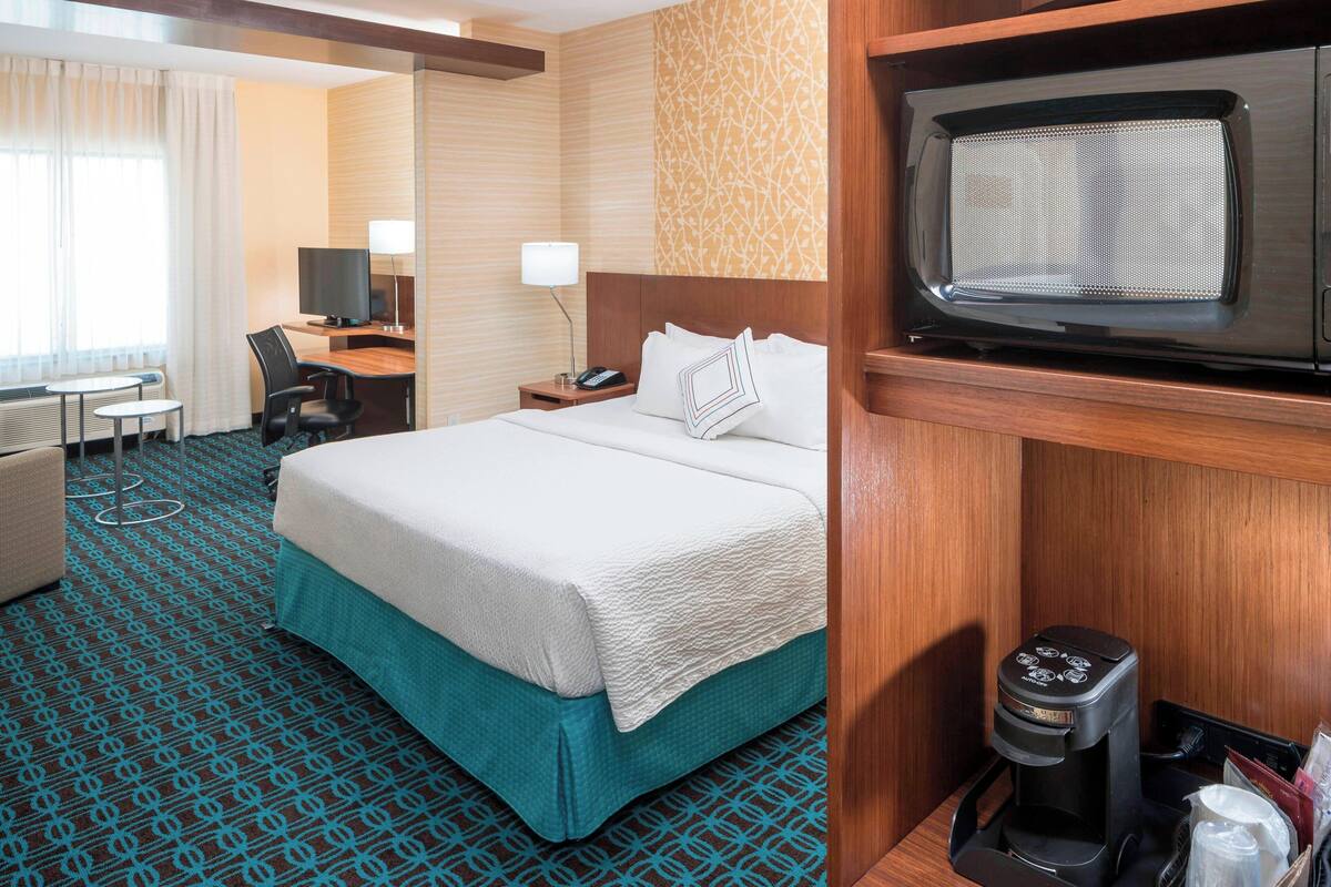 A hotel room with a bed, a desk, a chair, a television, and a coffee maker.