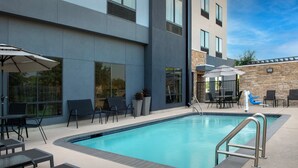 An outdoor swimming pool area with lounge chairs, umbrellas, and a modern building in the background. - Fairfield Inn & Suites by Marriott Houston Pasadena (Pasadena)
