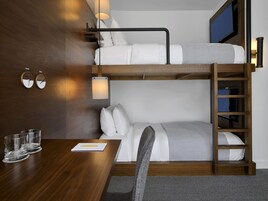 Ein Schlafraum mit Etagenbetten, einem Holztisch, zwei Nachttischen und einem an der Wand montierten Fernseher.