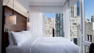 Habitación de hotel moderna con una cama grande, cabecero de madera y vistas a la ciudad a través de amplios ventanales.