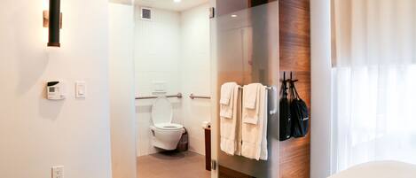 A modern bathroom with a glass shower enclosure, a toilet, and a towel rack with towels.