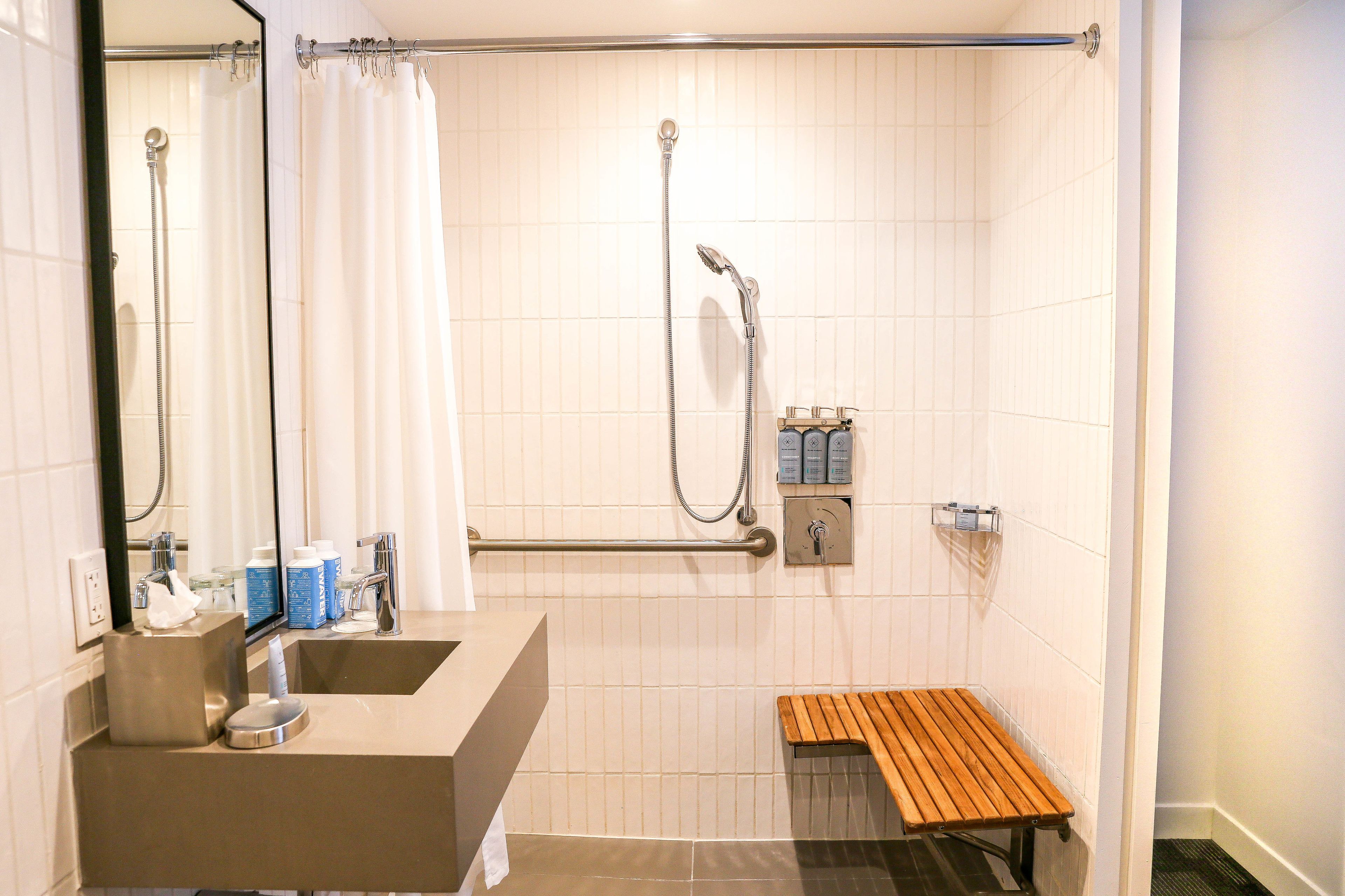 A modern bathroom with a shower, a sink, a mirror, and a wooden bench.