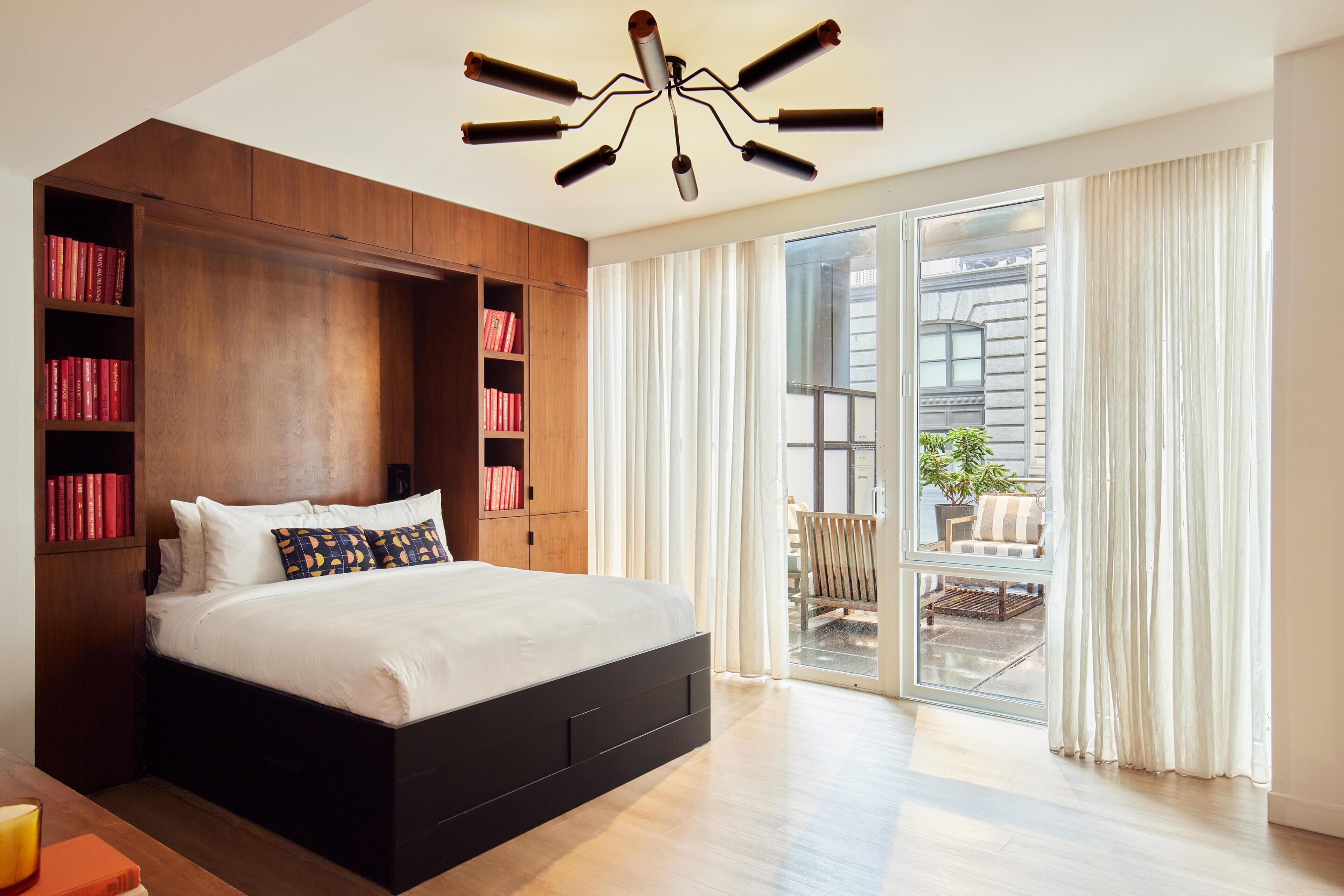 A modern bedroom with a large bed, built-in bookshelves, and a sliding glass door to a balcony.