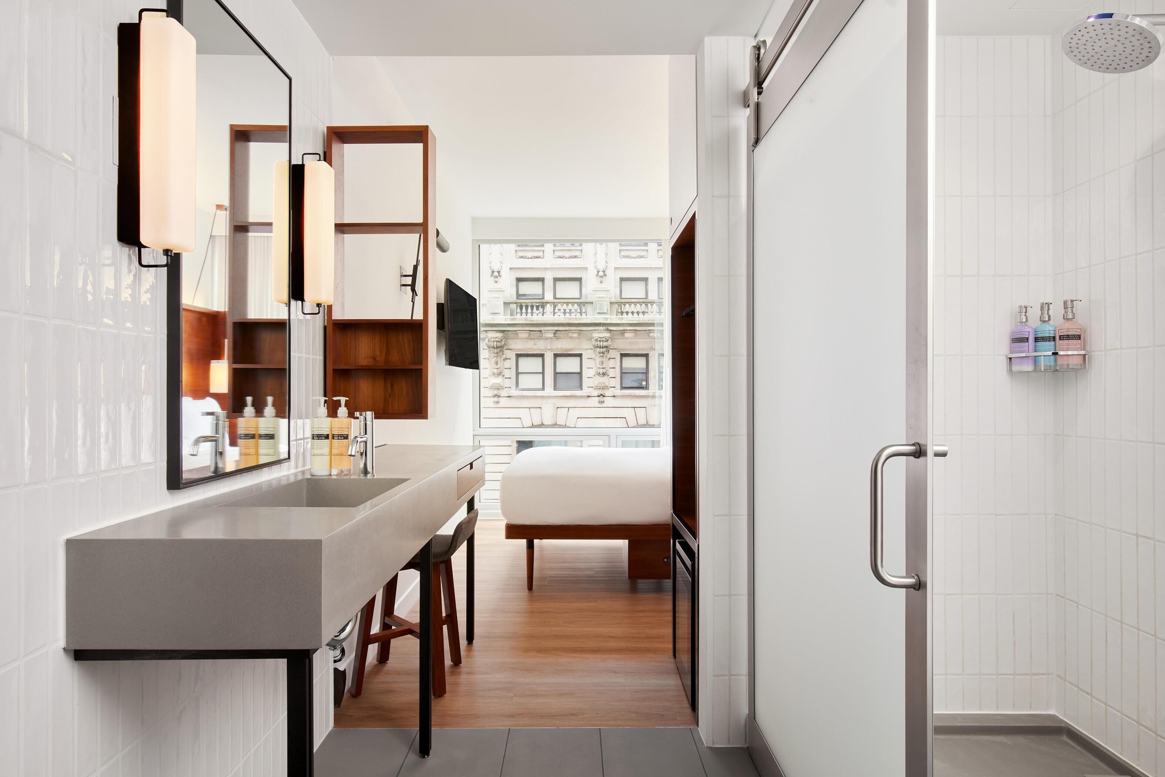 Un baño moderno con un espejo grande, una ducha y vistas a un edificio a través del ventanal.