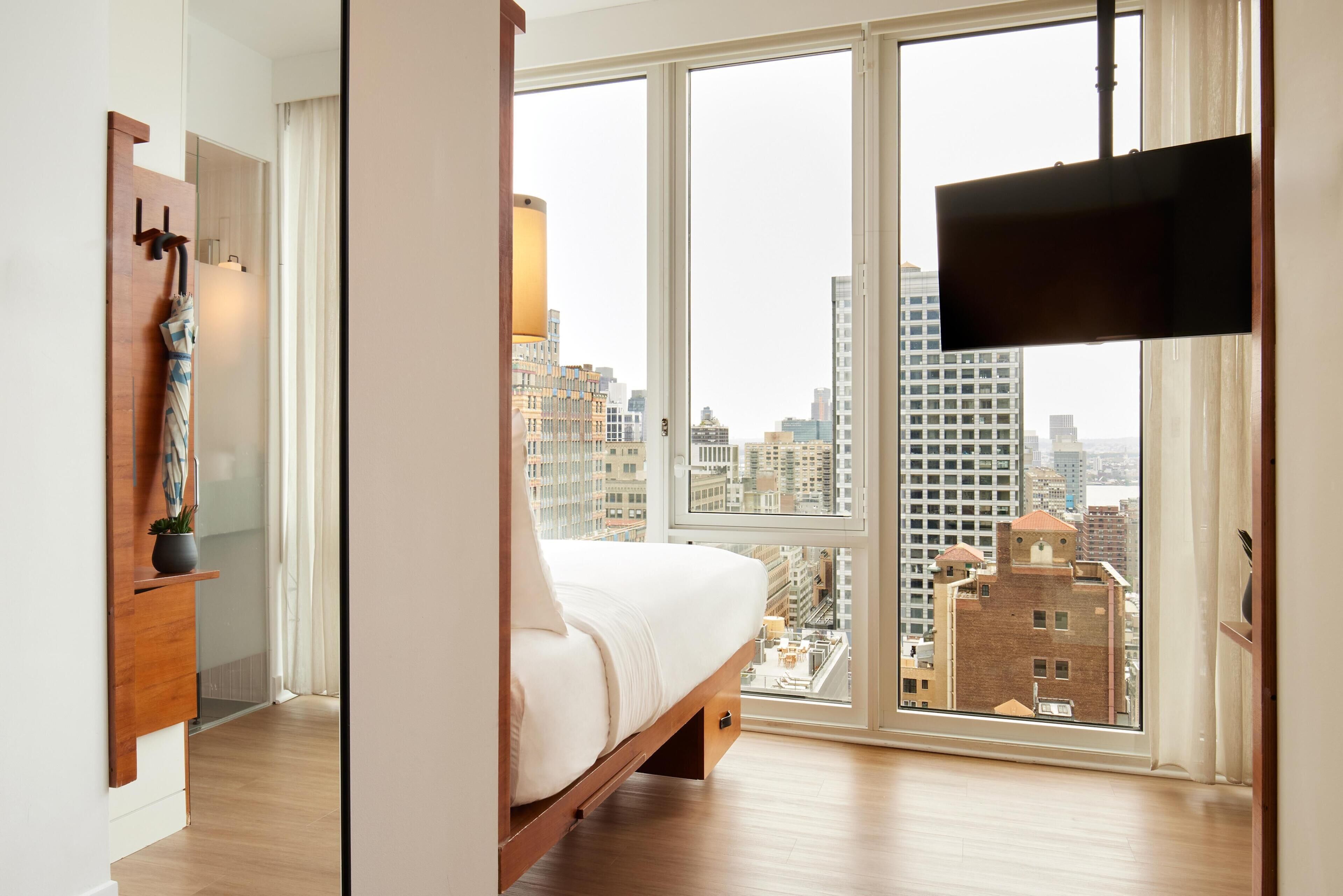 A bedroom with a large window, a bed, a TV, and a wooden cabinet.