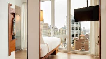 A bedroom with a large window, a bed, a TV, and a wooden cabinet.