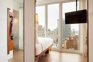 A bedroom with a large window, a bed, a TV, and a wooden cabinet. - Arlo NoMad (New York)