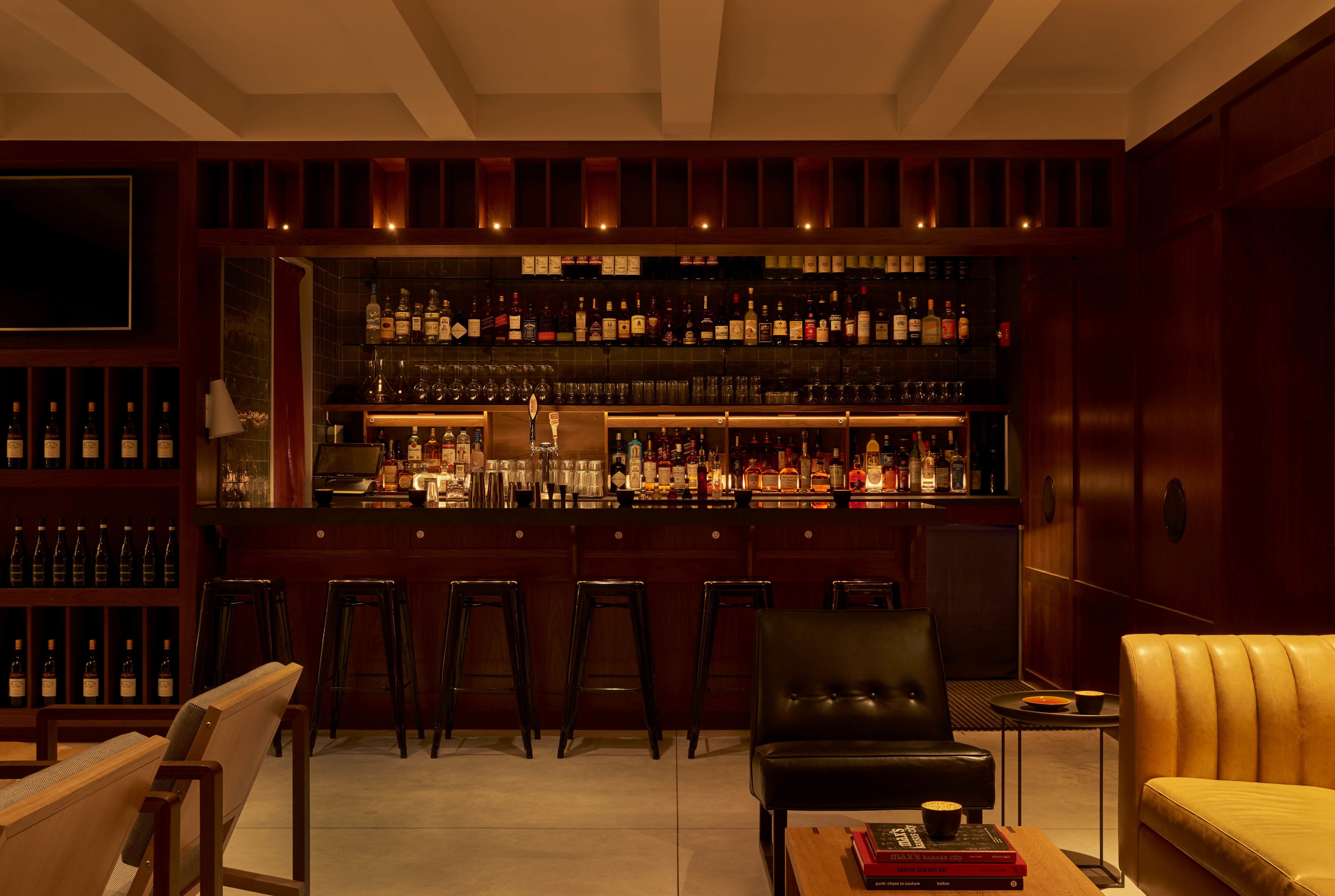 A bar area with multiple stools, a bar counter, and shelves stocked with bottles.