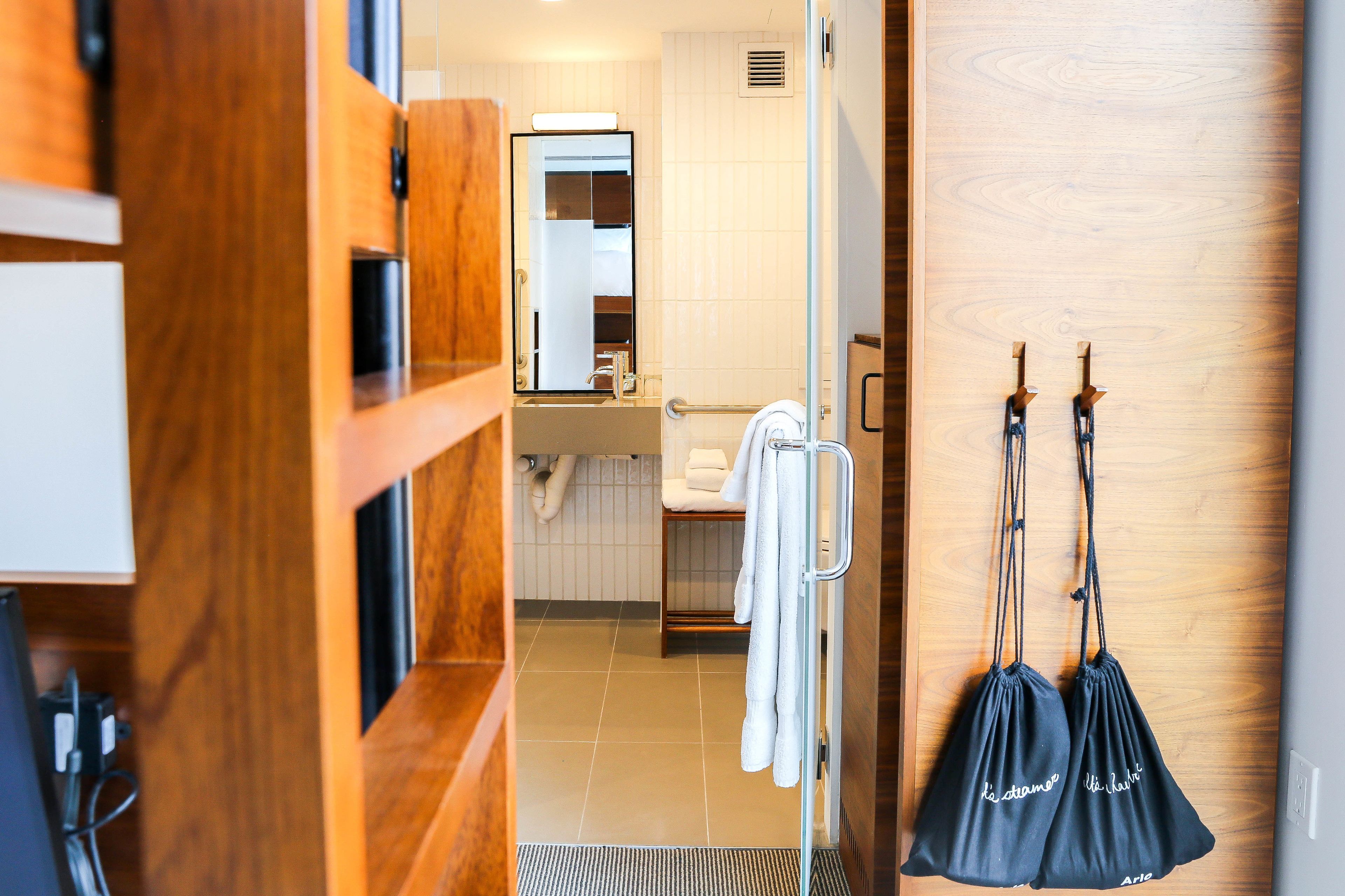 A hotel bathroom with a wooden vanity, a mirror, a towel rack, and a shower area.