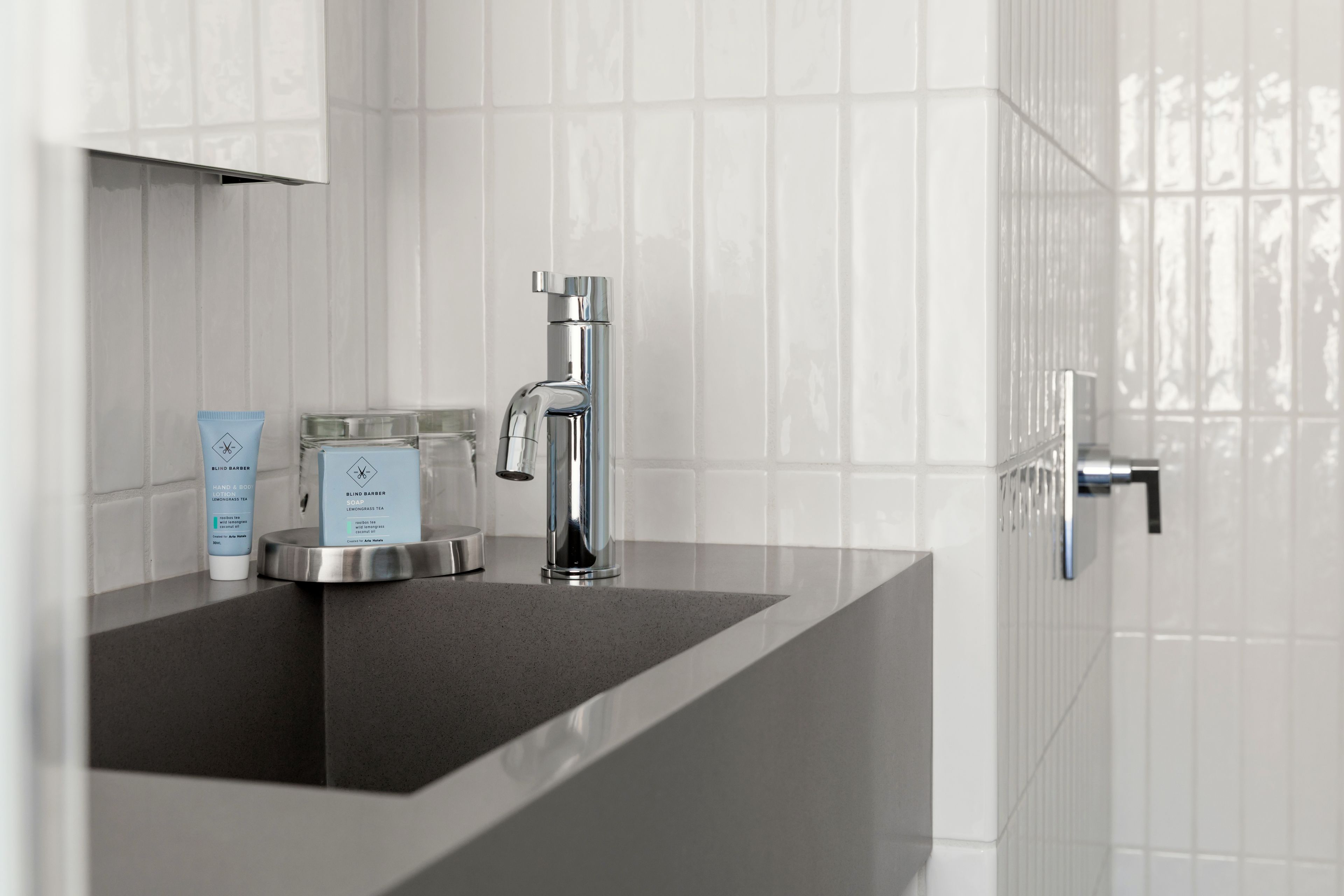 A modern bathroom with a chrome faucet, a black countertop, and white tiled walls.