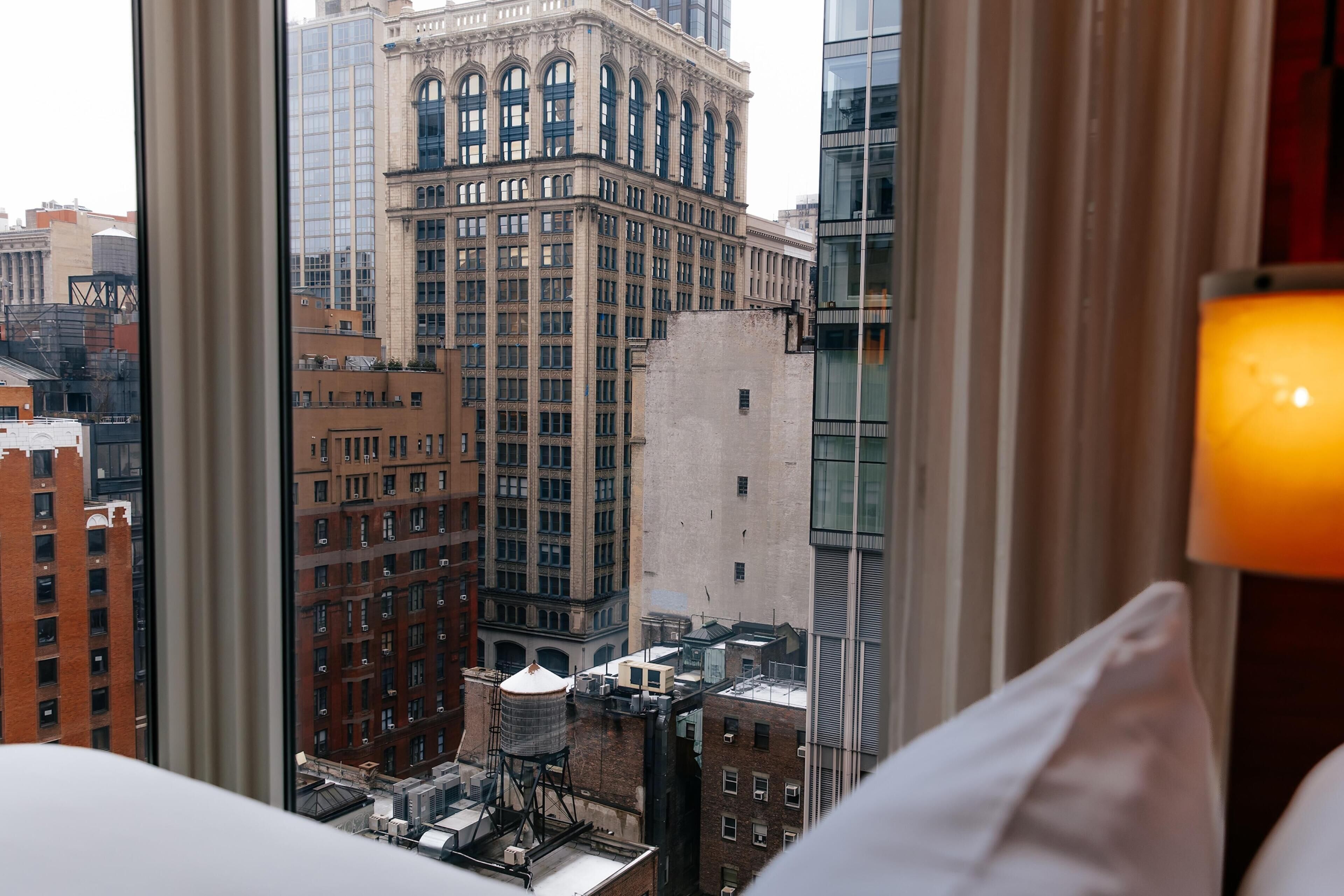 Une chambre d’hôtel avec vue sur le paysage urbain, comprenant un bâtiment historique doté de fenêtres en arc de cercle et un bâtiment moderne en verre.