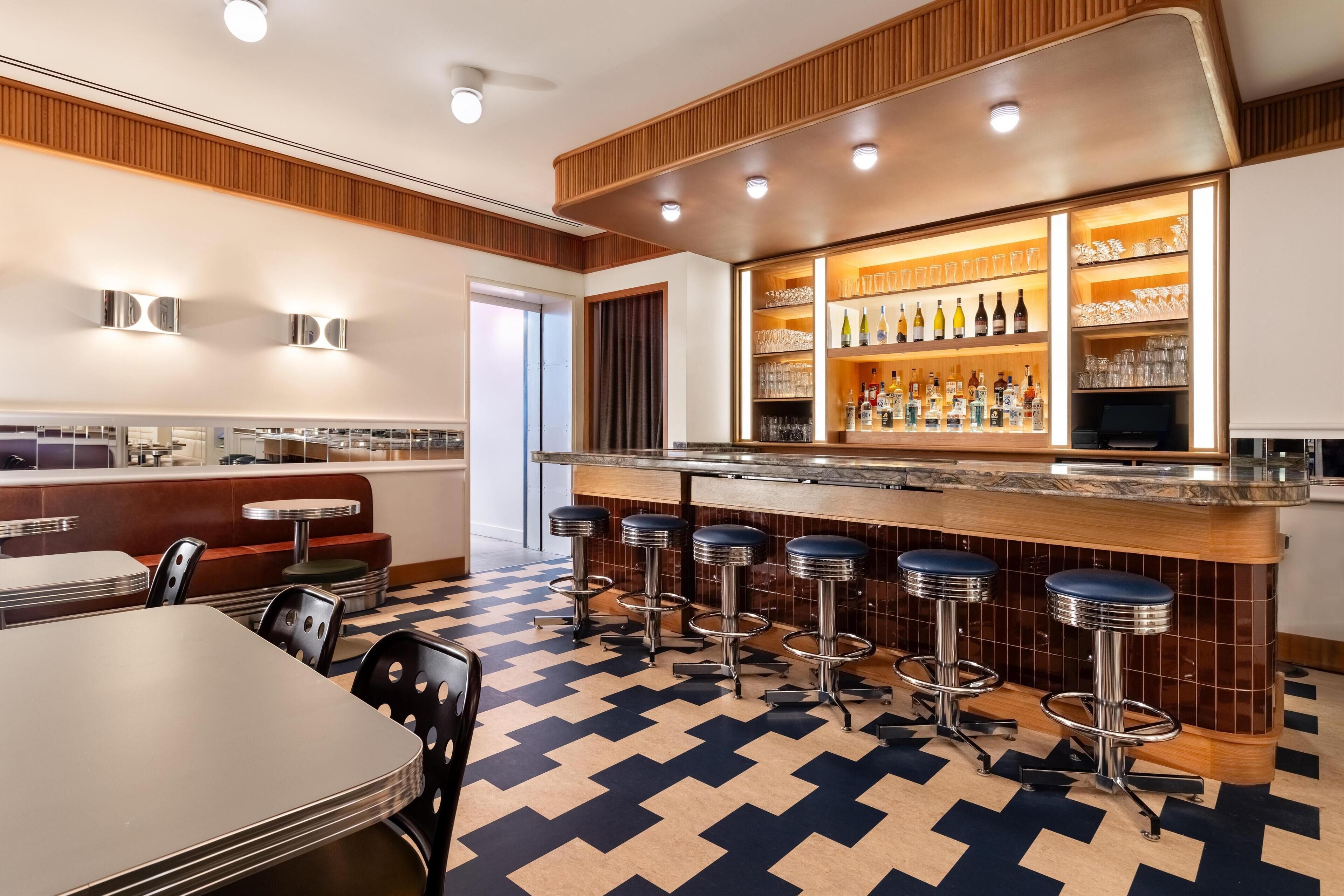 A bar area with stools, a counter, and shelves with bottles and glasses.