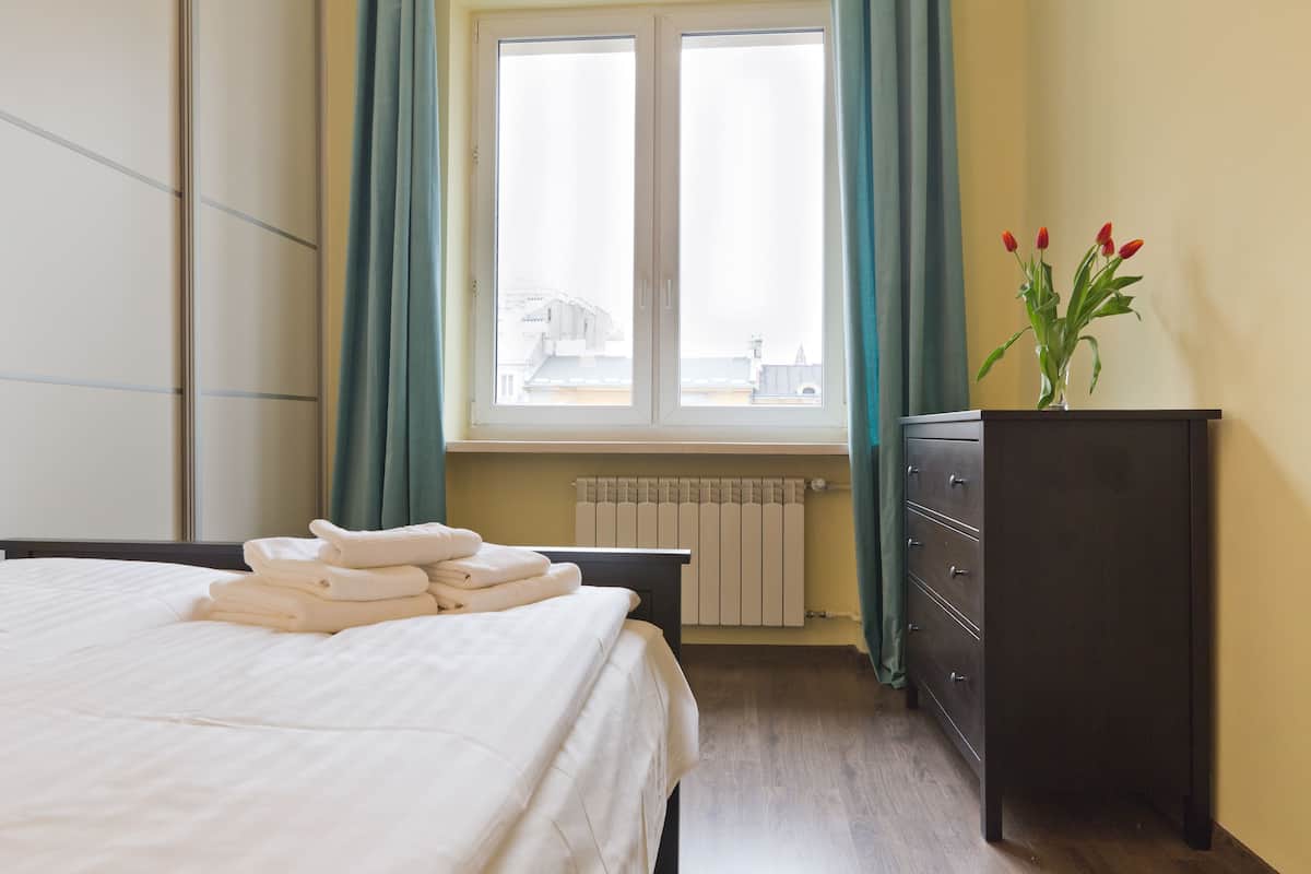 A hotel room with a bed, a dresser, a window with curtains, and a radiator.