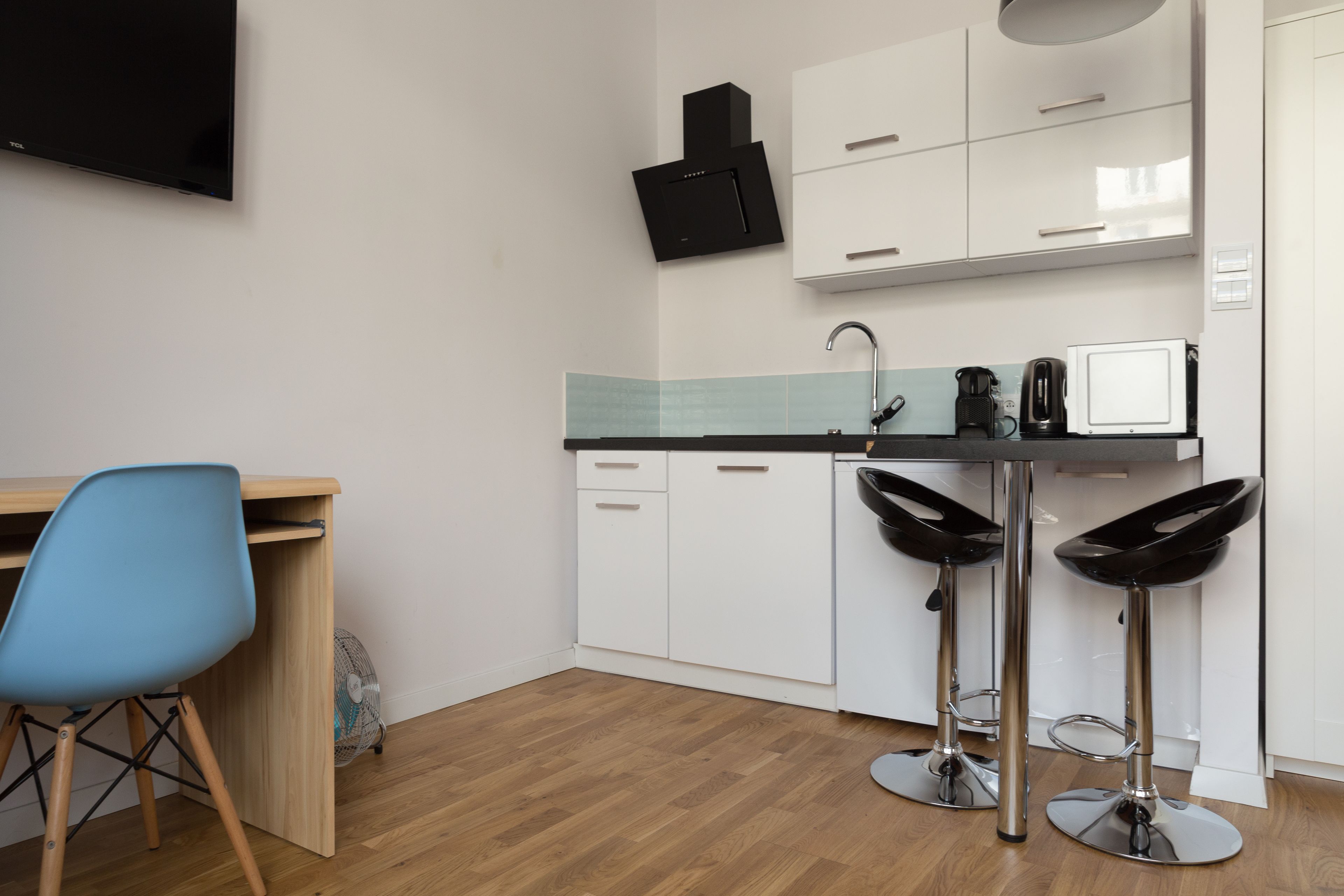 Een moderne keuken met witte kasten, een zwarte afzuigkap, een spoelbak en twee zwarte barkrukken.