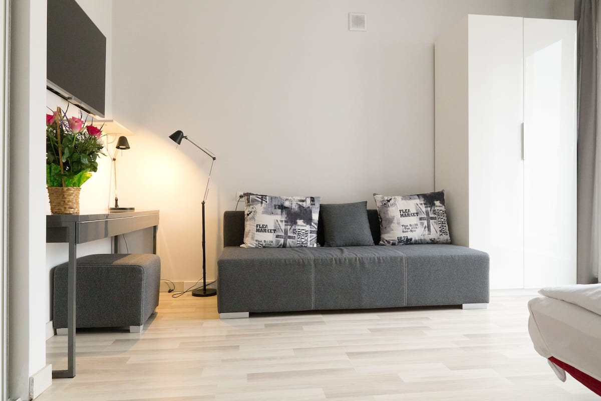 A modern living room with a grey sofa, a small ottoman, a standing lamp, and a side table with a plant.