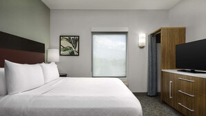 Habitación de hotel con una cama grande, televisor de pantalla plana, mueble de madera, ventana con vistas y una lámpara fijada a la pared.