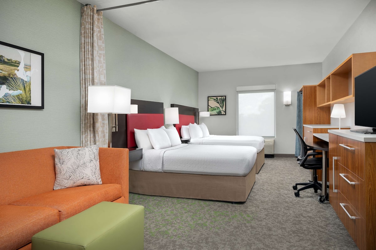 A hotel room with two beds, a sofa, a desk, and a television.