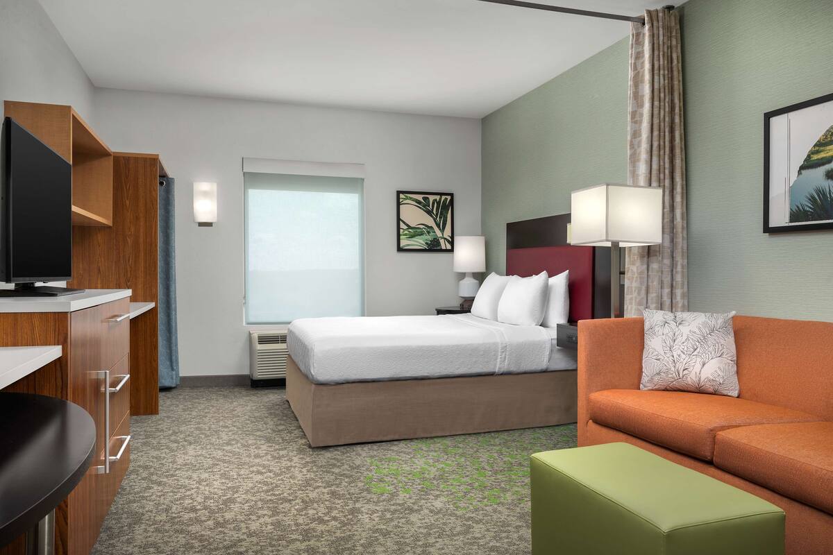 A hotel room with a bed, a sofa, a desk, and a TV.