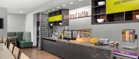 A modern breakfast bar with a 'Good Morning' sign, a 'Inspired Table' sign, and a yogurt/milk dispenser.