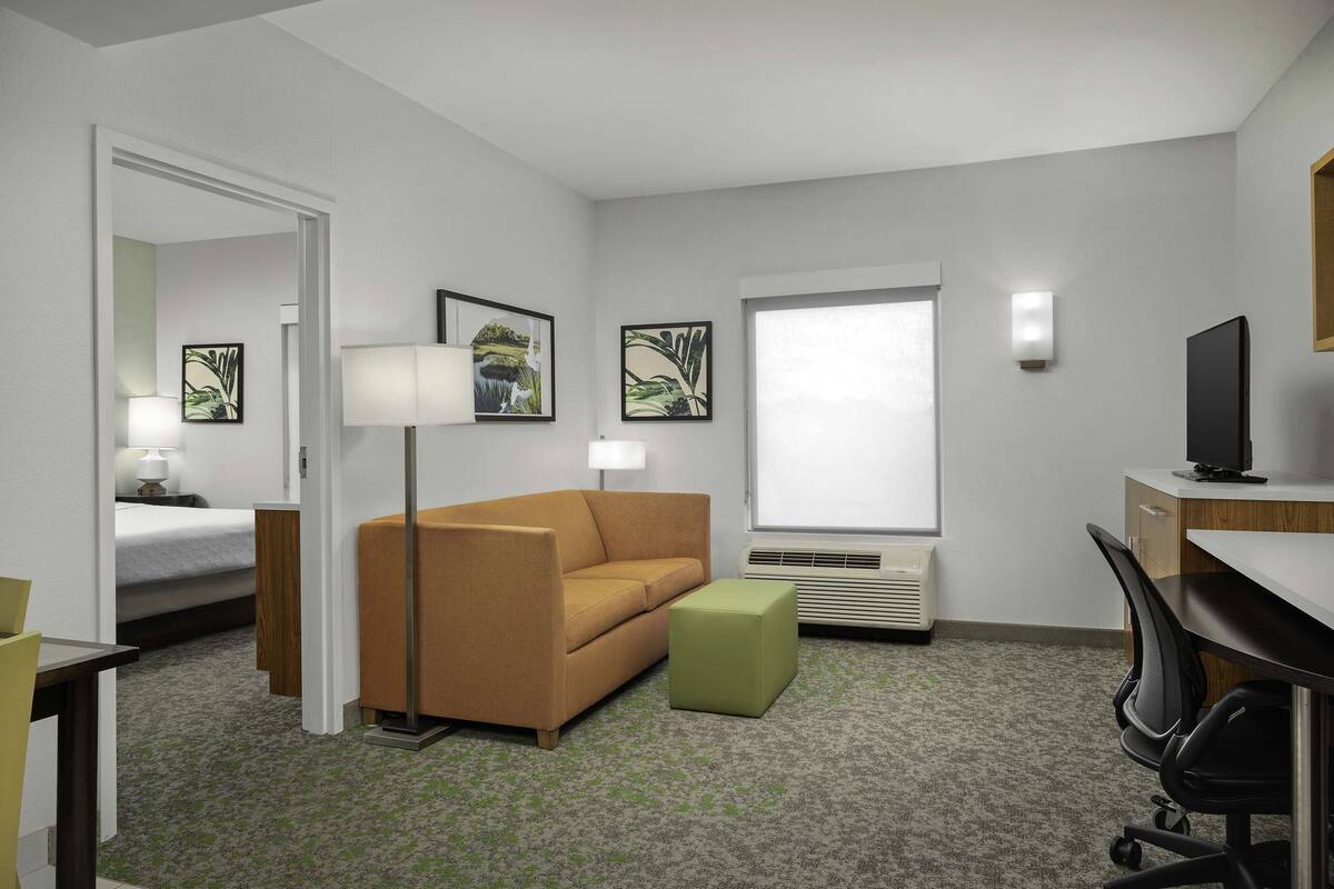 A hotel room with a bed, a sofa, a desk, a chair, a lamp, a television, and framed pictures on the wall.