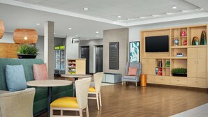Un moderno vestíbulo de hotel con zonas de estar, televisión y un bar de bebidas.