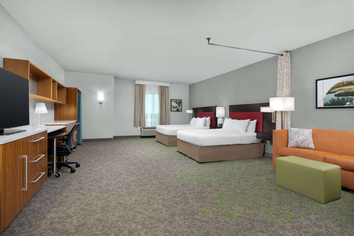 A hotel room with a desk, two beds, a sofa, and a TV.