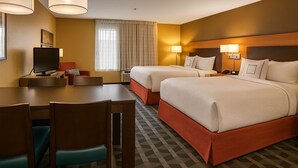 Une chambre d’hôtel avec deux lits, un bureau, des chaises, une télévision et une fenêtre avec des rideaux.