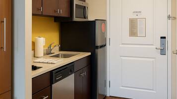 Una cocina compacta con armarios de madera, microondas, refrigerador y lavavajillas.