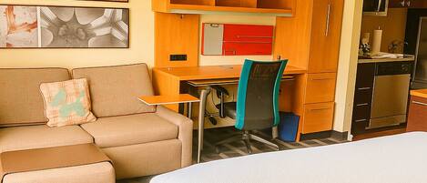 A hotel room with a bed, a sofa, a desk, and a kitchenette.