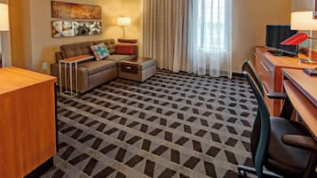 Habitación de hotel con sofá, escritorio, ordenador y alfombra estampada.