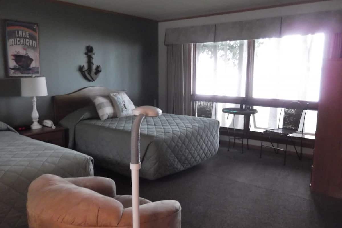 A hotel room with two beds, a chair, a table, and a window with curtains.