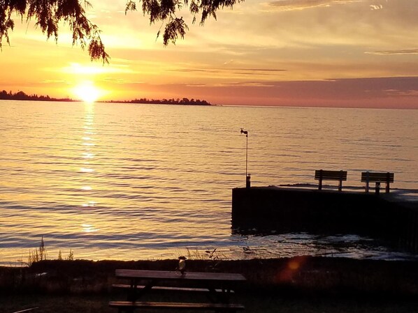 A sunset over a calm body of water with a dock, benches, and a picnic table.