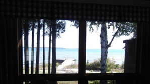 A room with a large window overlooking a beach and the sea. There is a table and a chair in the foreground. - Square Rigger Harbor Motel (Baileys Harbor)