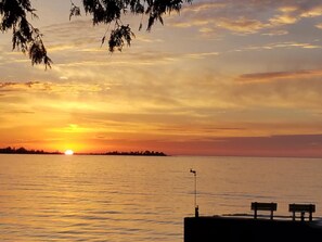A sunset over a calm body of water with a dock and benches. - Square Rigger Harbor Motel (Baileys Harbor)