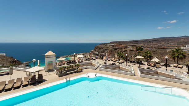 Un espace piscine avec des chaises longues et des parasols, un petit bâtiment et une vue sur la mer.