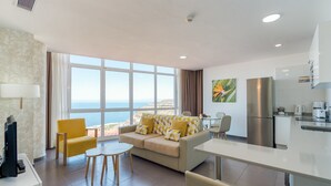 Une chambre d’hôtel moderne avec un canapé, des fauteuils jaunes, une table à manger et un coin cuisine.