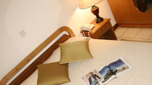 A neatly made bed with a wooden headboard, a bedside lamp, a telephone, and a magazine on the bed. - Sunshine Hotel (Asmara)