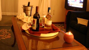 A room with a wooden table set with a bottle, glasses, and a candle. There is a television on a stand and a couch in the background. - Sunshine Hotel (Asmara)