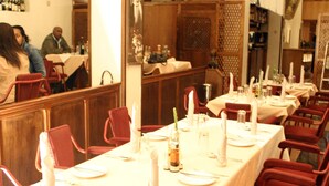 A restaurant with multiple tables set for dining, red chairs, and a person in the background. - Sunshine Hotel (Asmara)
