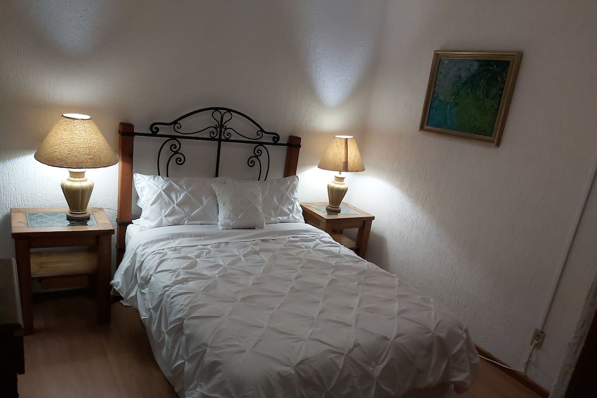 Ein ordentlich bezogenes Bett mit weißer Bettwäsche, zwei Nachttischlampen und ein Bild an der Wand.