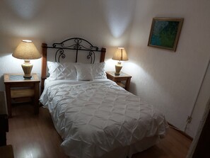 Ein ordentlich bezogenes Bett mit weißer Bettwäsche, zwei Nachttischlampen und ein Bild an der Wand.