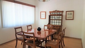 Comedor con una mesa y sillas de madera, un florero sobre la mesa y una ventana con persianas.