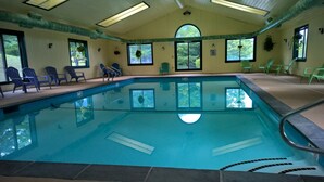 An indoor swimming pool with clear water, surrounded by green chairs and large windows offering views of trees. - Winterplace at Okemo, A Vail Resorts Property (Ludlow)