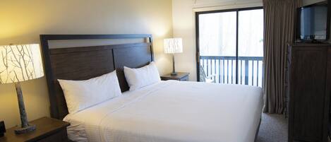 A hotel room with a large bed, a nightstand with a lamp, a dresser, and a television on a cabinet.