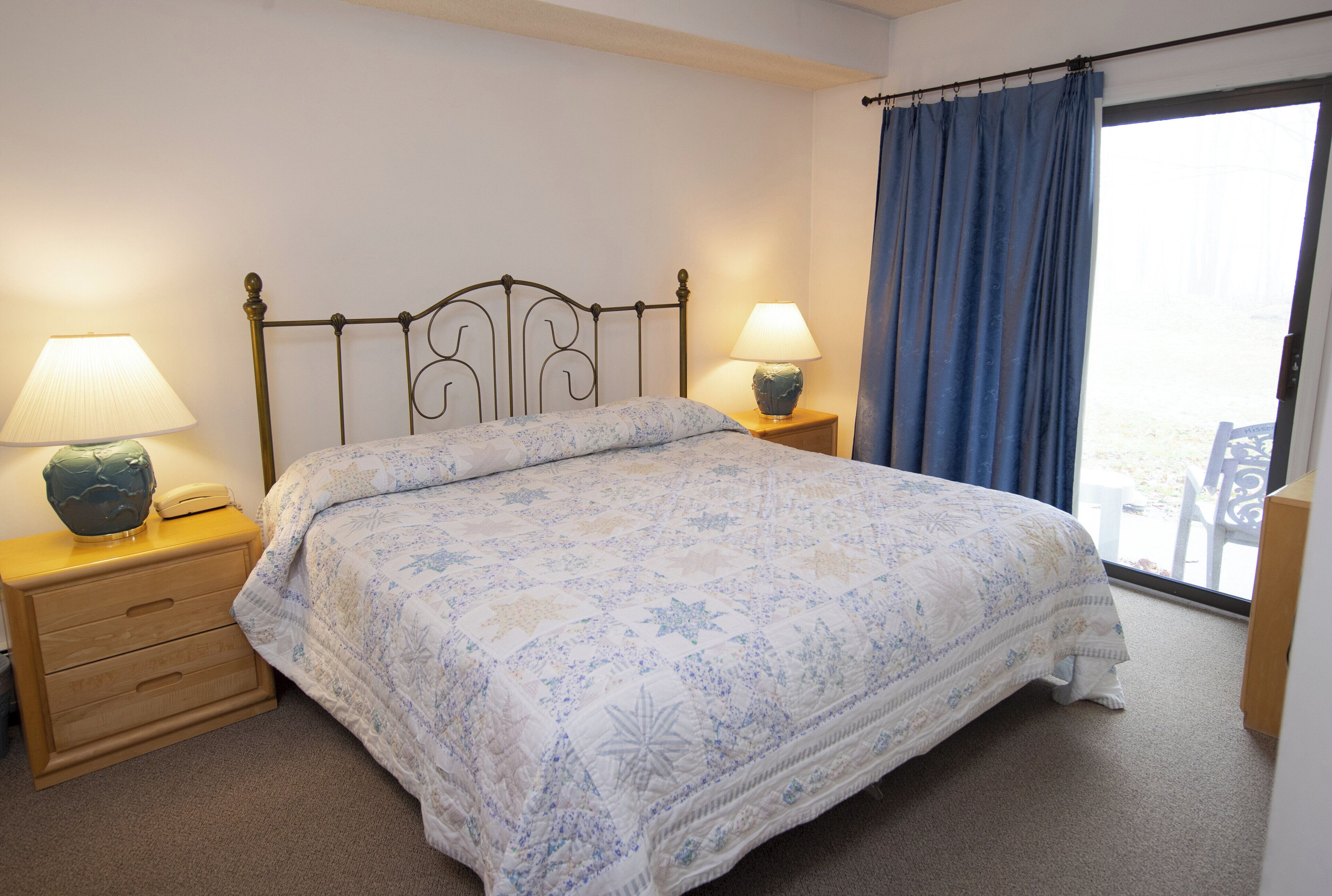 Una cama bien hecha con una colcha floral, dos lámparas de noche y una mesita de noche de madera.