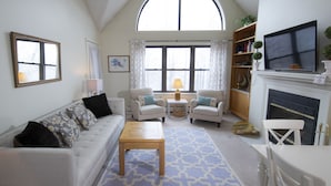 A living room with a high arched window, a fireplace, a television, and a bookshelf. - Winterplace at Okemo, A Vail Resorts Property (Ludlow)