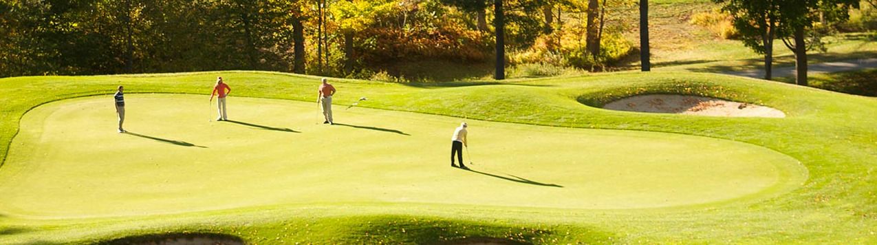 Un parcours de golf avec un gazon bien entretenu, des bunkers de sable et des arbres en arrière-plan.