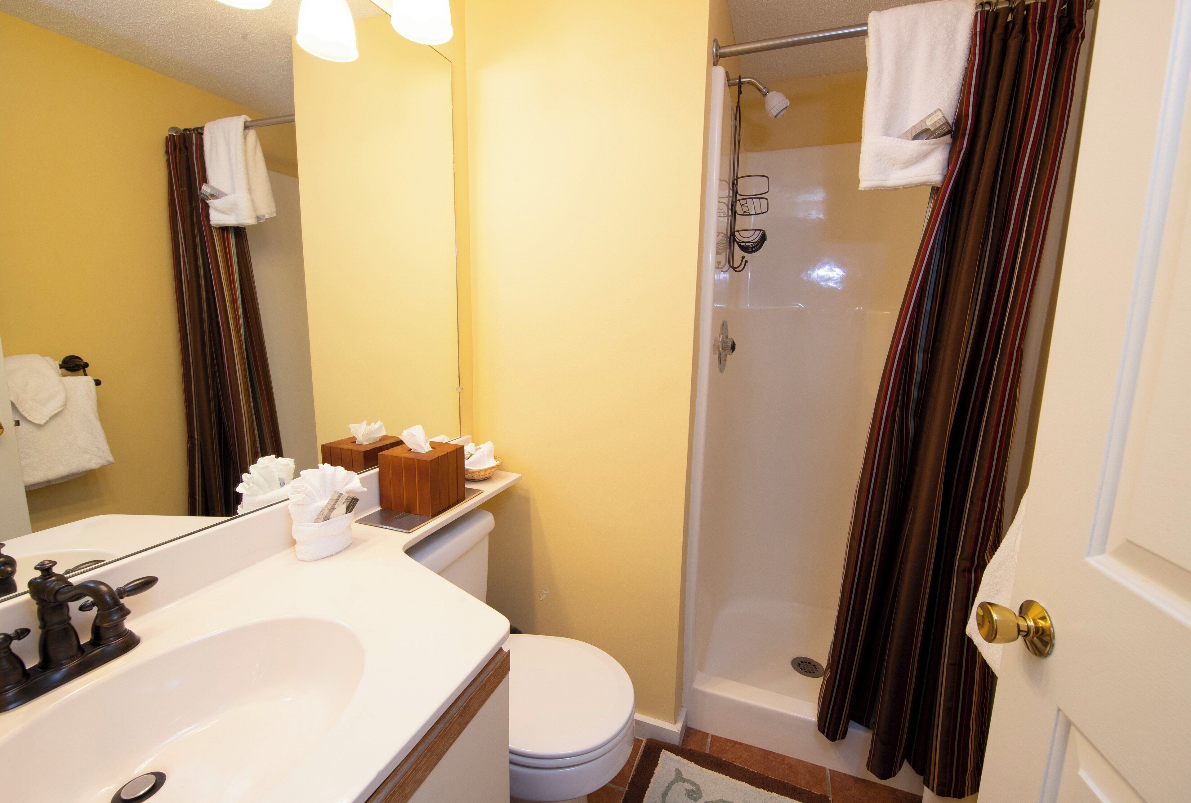 Een badkamer met een witte wastafel, toilet en douche. Handdoeken hangen aan de douchegordijnstang en er is een handdoekrek in de douche.