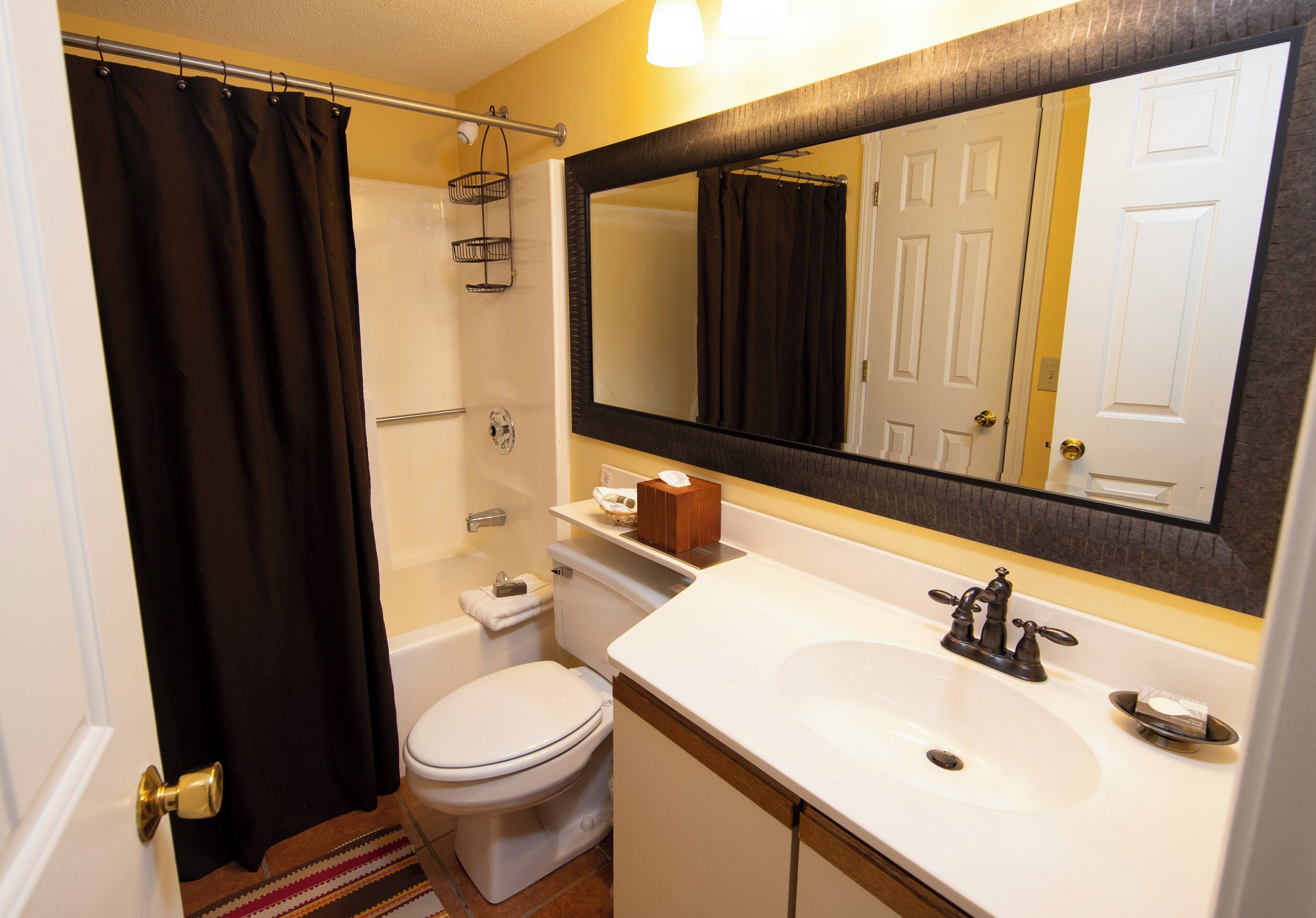 A bathroom with a white sink, a large mirror, a toilet, and a shower curtain.