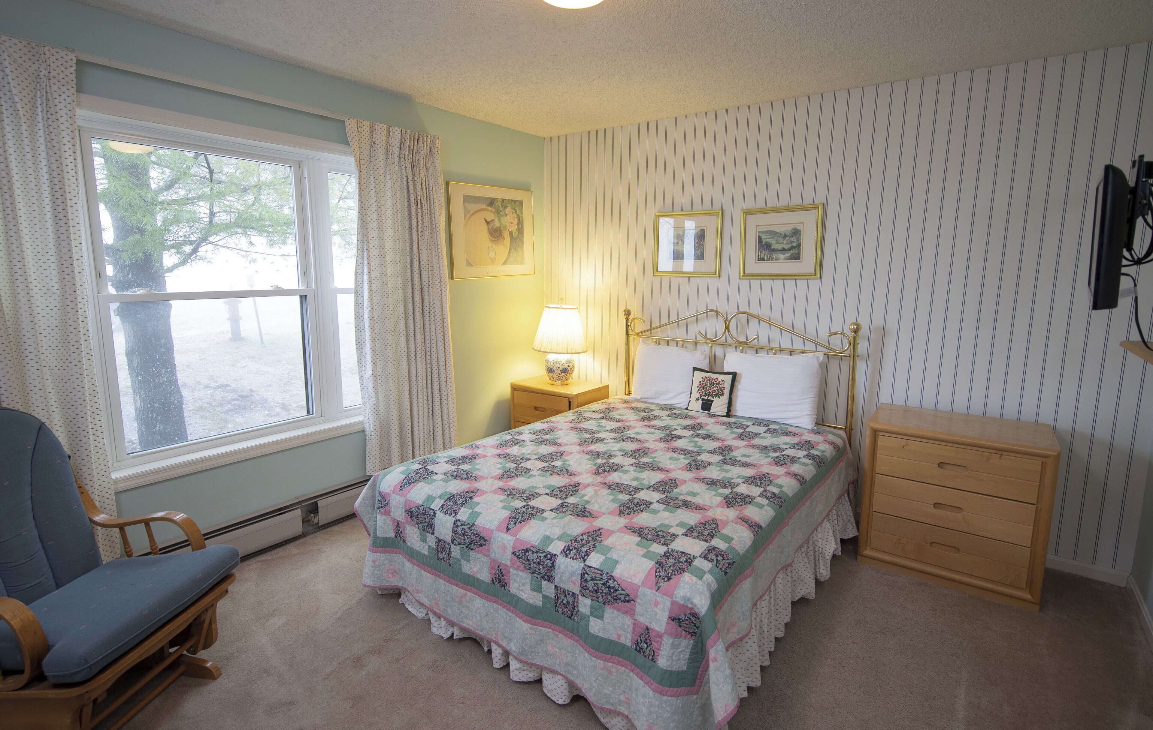 A bedroom with a bed, a chair, a nightstand, and a dresser.